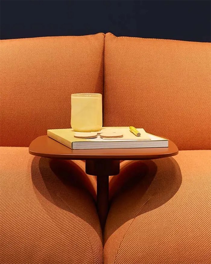 Integrierter Beistelltisch im Jalis Flow – Design trifft auf Alltagstauglichkeit Nahaufnahme eines integrierten Beistelltischs zwischen zwei orangefarbenen Sitzmodulen des Jalis Flow von COR. Auf dem Tisch stehen ein gelbes Glas, ein Notizbuch und ein Stift – ein stilvolles Detail, das Funktionalität und Design harmonisch verbindet.