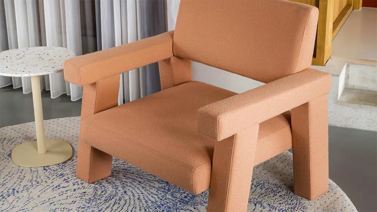 Minimalistischer Lounge-Sessel „Mohs Chair“ von Philip Bogaerts in terracottafarbenem Wollbezug, mit geometrischer Form und markanten, breiten Armlehnen auf einem gemusterten Teppich.