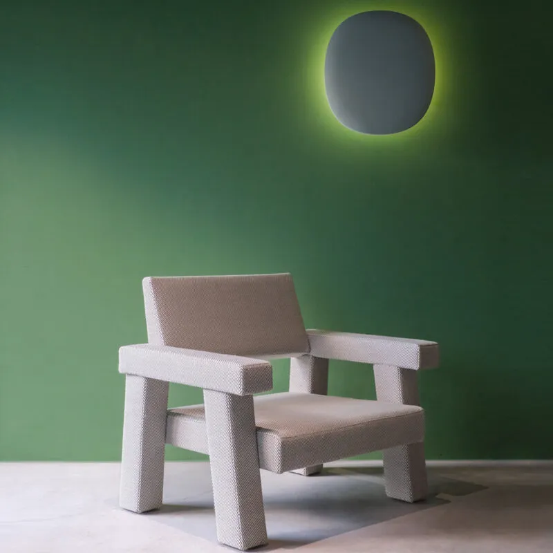 Mohs Chair von Bogaerts – modernes Designobjekt Hellgrauer Mohs Chair von Philip Bogaerts mit strukturierter Wolloberfläche, inszeniert vor einer grünen Wand mit leuchtendem Wandelement – minimalistisches Design mit skulpturaler Wirkung.