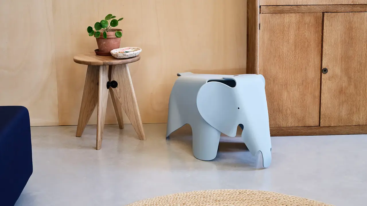 Hellblauer Eames Elephant von Vitra aus Kunststoff in einem minimalistischen Interieur mit Holzmöbeln und Pflanzen, dekorativ platziert neben einem Beistelltisch.