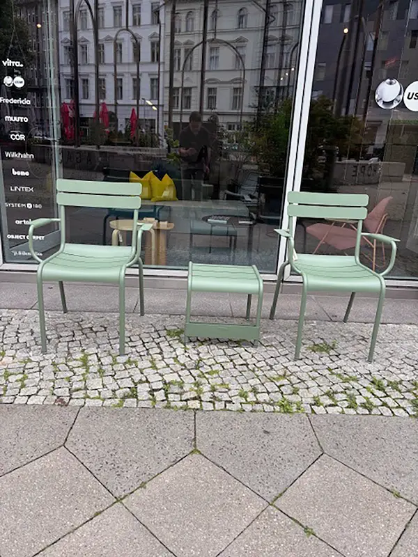 Fermob Luxembourg Sitzgruppe vor dem Showroom in Berlin-Mitte Zwei grüne Luxembourg-Armlehnstühle und ein passender niedriger Tisch von Fermob auf dem Gehweg vor dem UnitedSpaces-Showroom mit Glasfassade und Markenübersicht im Hintergrund