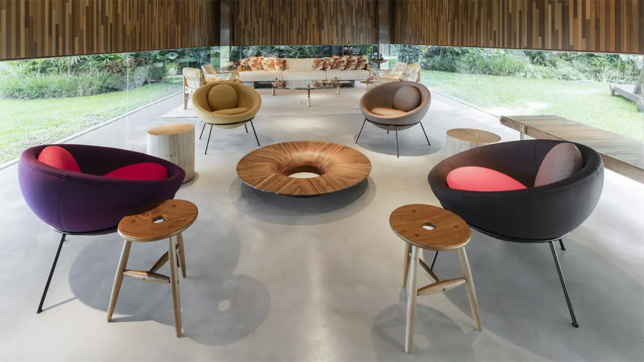 Mehrere farbige Bardi’s Bowl Chairs von Arper in einem hellen Raum mit großen Glasfronten, ergänzt durch runde Holztische und Hocker – ein Beispiel für modernes, flexibles Interior Design.