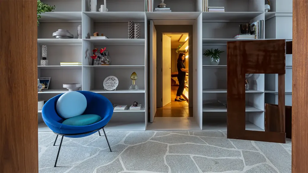 Ein blauer Bardi’s Bowl Chair von Arper vor einer großen Regalwand, mit Blick in einen angrenzenden Raum – ein Designakzent, der Lebendigkeit und Stil ins Interieur bringt.