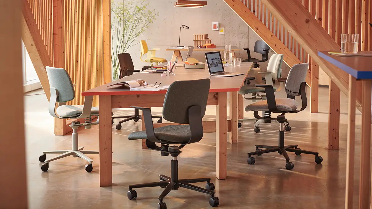 Moderne Büroeinrichtung mit mehreren Wilkhahn WiChair Drehstühlen an Holztischen in einem offenen, lichtdurchfluteten Arbeitsbereich.