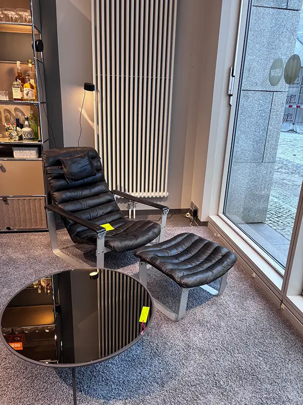 Archive Sale bei unitedspaces – Loungechair mit Ottoman im Showroom Schwarzer Loungechair mit passendem Ottoman als Ausstellungsstück im Archive Sale Showroom von unitedspaces nahe der Fensterfront