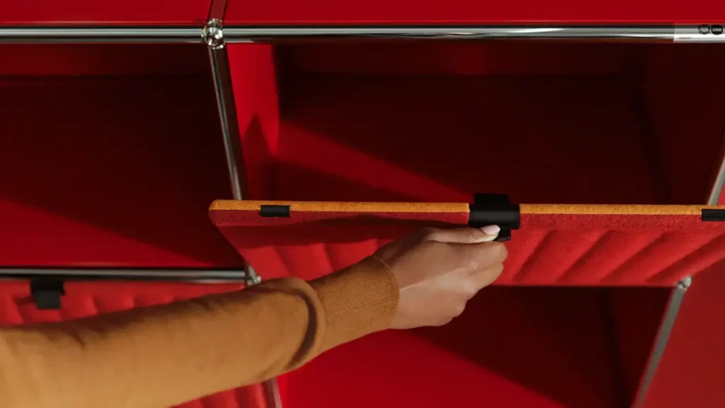 Hand montiert ein rotes USM Haller Soft Panel magnetisch an der Unterseite eines USM Regalelements